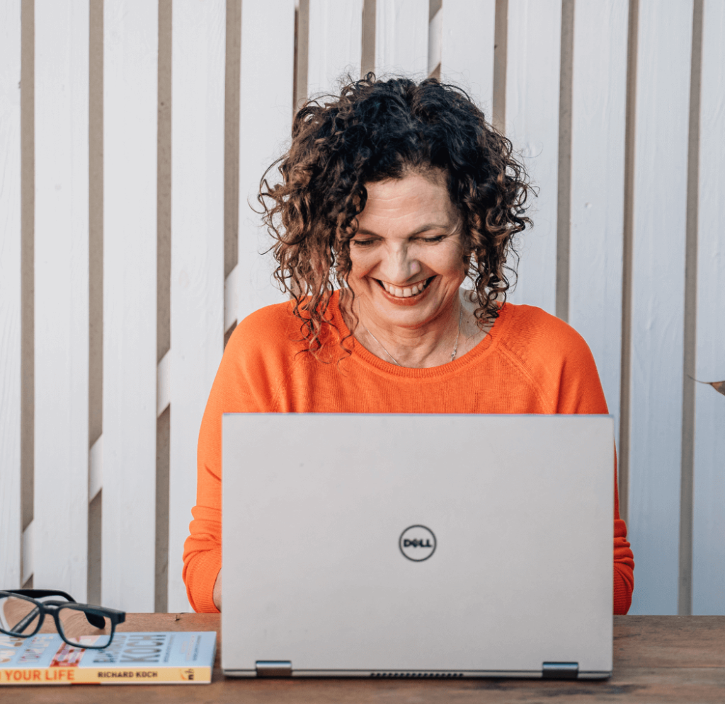Sue in an orange top smiling and looking down at a laptop in front of her